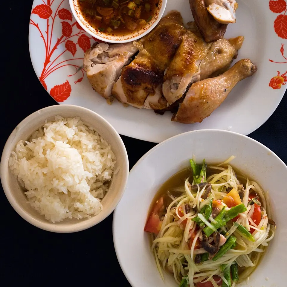A plate of green papaya salad beside a bowl of sticky rice and grilled chicken