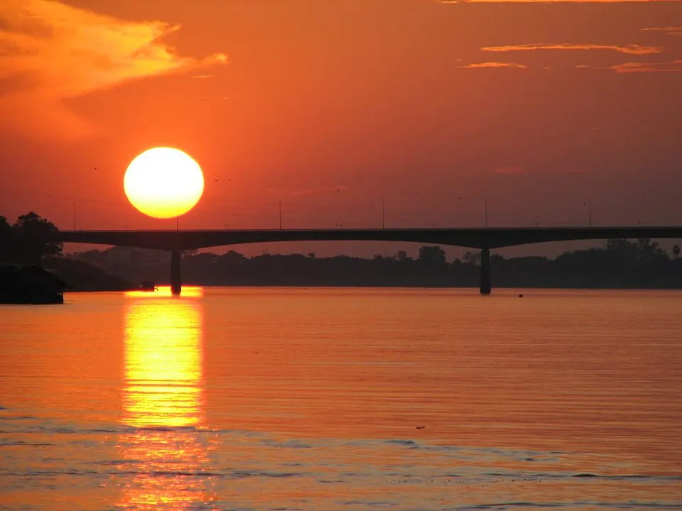 An orange sun setting over the Mekong with a bridge in silhouette